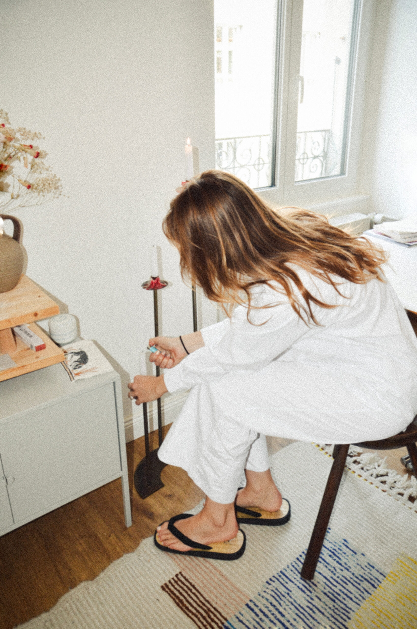 Young woman sitting on chair and hunching down to the floor and lighting a candle with her back to the camera